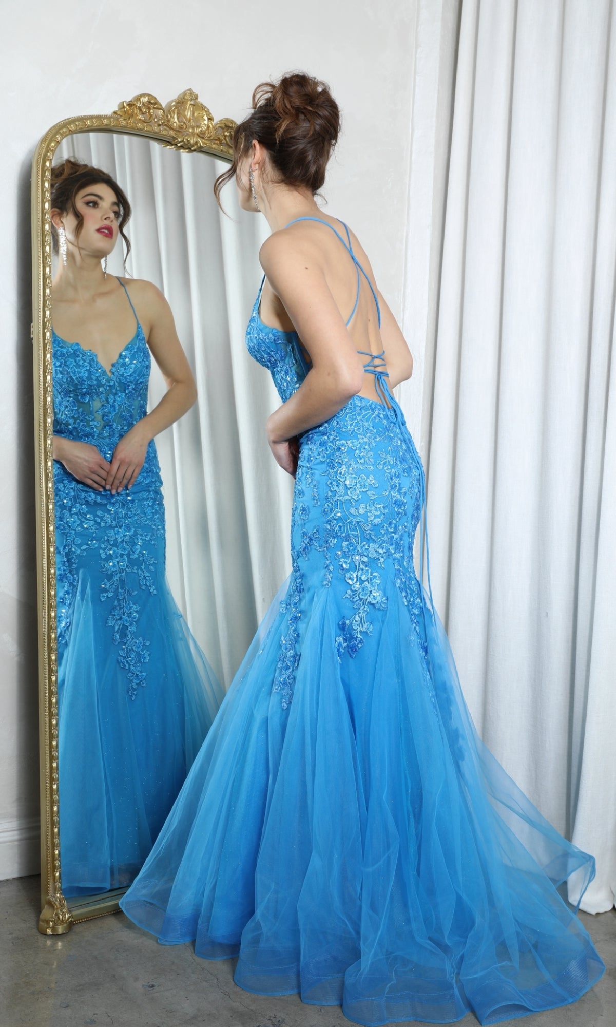 A woman stands before a tall mirror in the Eureka 9696 Sequin-Floral Long Mermaid Prom Dress, featuring sparkling floral embroidery on the fitted bodice and a dramatic flared tulle skirt.
